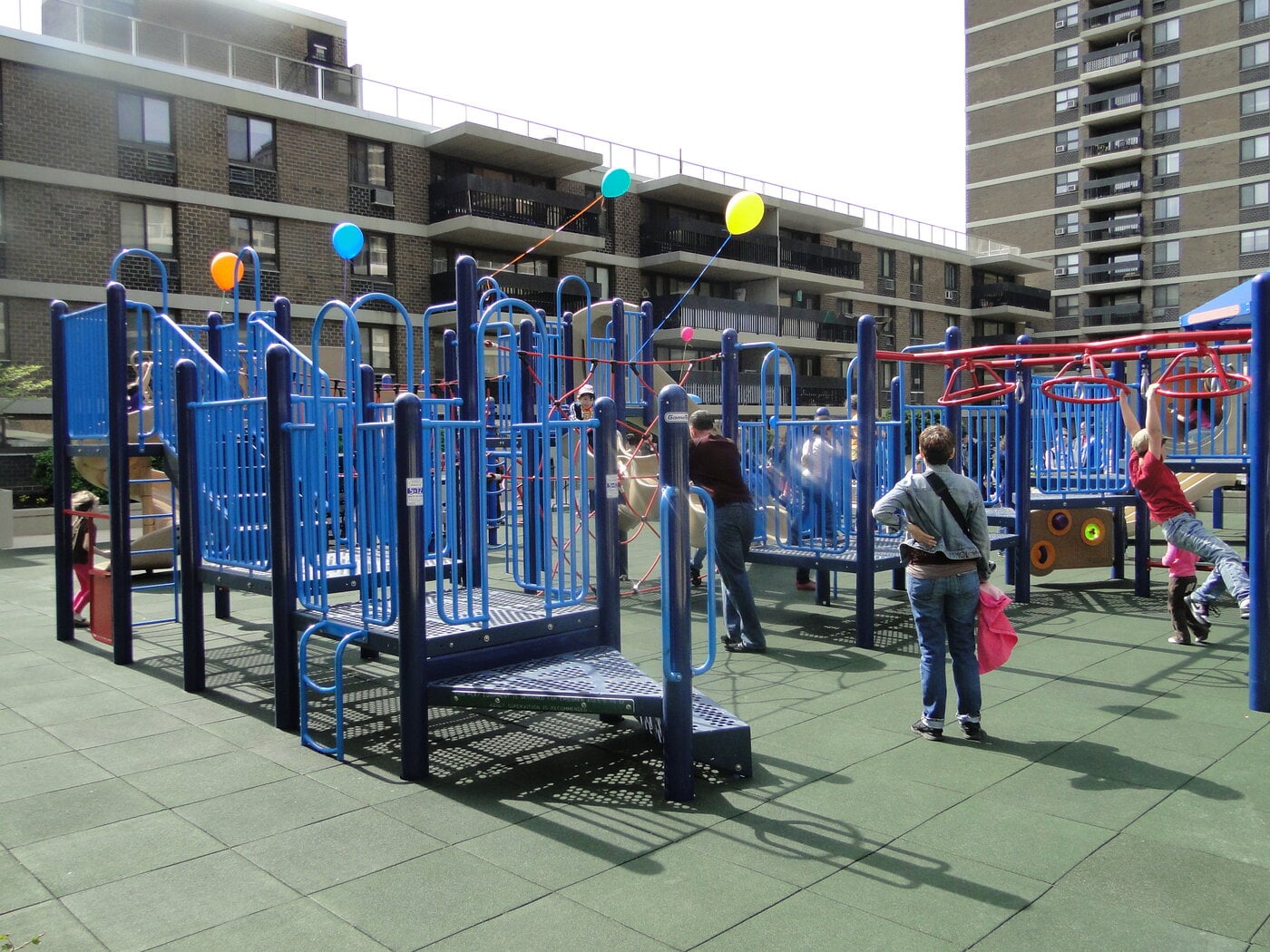 Ground-level view of the playground's blue climbing structures, with kids playing on a sunny day